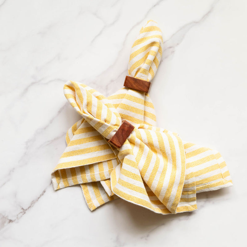 Yellow and white striped napkin with wooden napkin rings on a marble surface