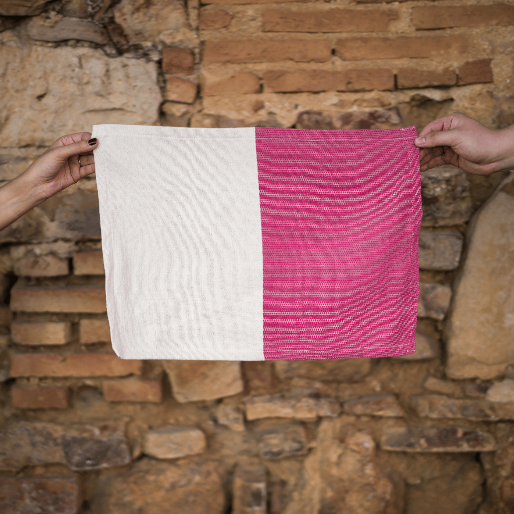 Handwoven Placemat in Rosa Mexicano (magenta pink) with neutral two-tone held up against a brick wall in Oaxaca, Mexico