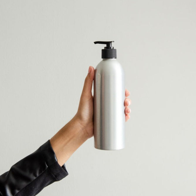 A woman's hand holding a Refillable Body Wash in Cucumber Melon Scent in Aluminum Pump Bottle with Black Pump