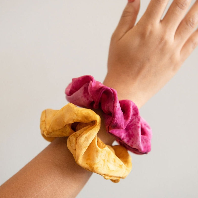 A hand holding with a pink and mustard yellow silk scrunchie hair tie on the wrist