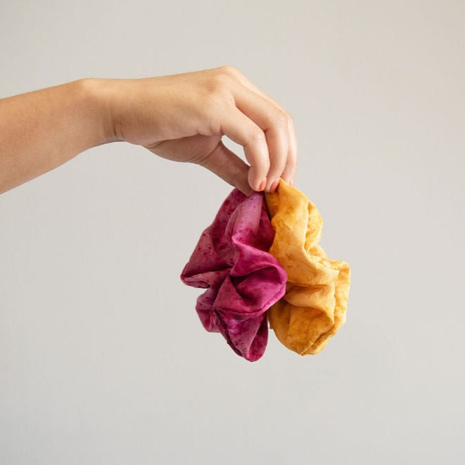 A hand holding a pink and mustard yellow silk scrunchie hair tie
